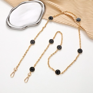 Detail of a golden chain with black smiley faces on beige fabric and metal tray