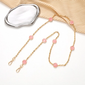 Detail of a gold crossbody chain with pink smiley faces and metal lobster clasps