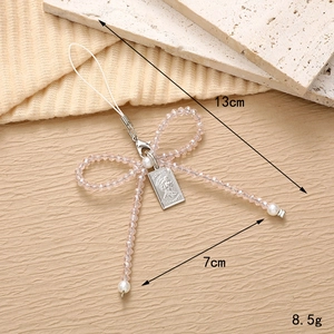 Pink beaded bow phone charm with pearls and silver coin tag on beige textured background