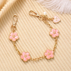Close-up of pink enamel floral phone chain with golden metal links and pearl heart charm