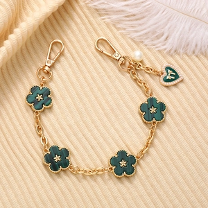 Detail of gold chain with green five-leaf flowers, heart pendant and white pearls