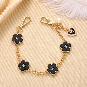 Detail of a gold-finish chain with black floral charms and a pearl on a beige fabric