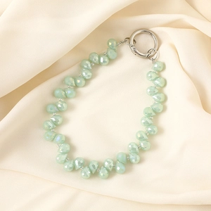 Close-up of light green teardrop crystal beads and silver ring clasp on beige fabric