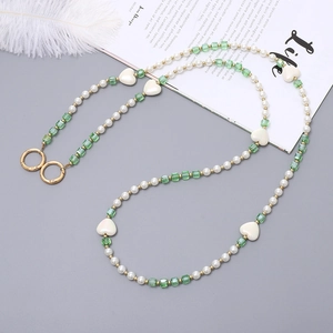 Détail de chaîne en perles et cristaux verts avec anneaux dorés sur un fond gris élégant