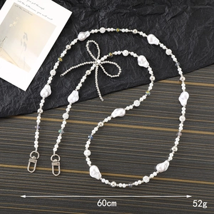 Crossbody pearl phone strap with bow detail and baroque pearls on textured backdrop