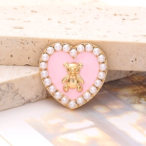 Macro shot of pink heart charm with gold bear relief and white pearl border on stone