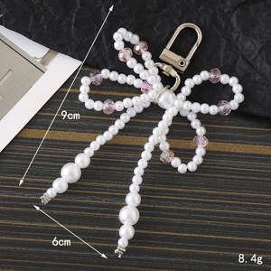 Handmade pearl bow keychain with pink crystal beads, 9cm height on textured background