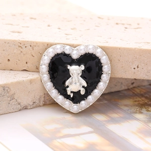 Macro shot of heart charm with black enamel, silver bear, and white pearl trim detail