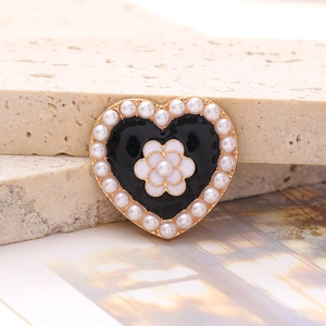 Macro detail of heart-shaped charm with black enamel, camellia flower, and pearls