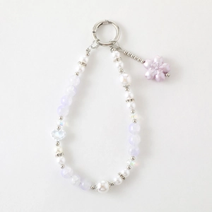 Détail d'un bijou de sac perlé avec pendentif fleur violette et anneau en métal argenté