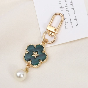 Detail view of flower pendant keychain with green petals and white pearl on fabric background