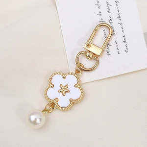 Detail of elegant gold flower keychain with white petals, star emblem, and pearl charm
