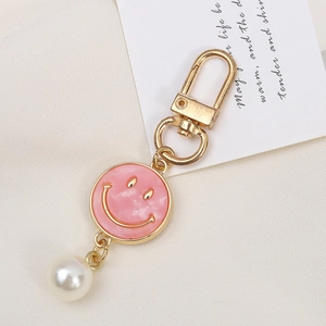 Pink marble smile face keychain with gold ring and white pearl on textured cloth