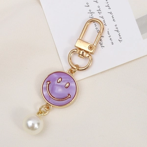 Close-up of golden alloy flower keychain with purple enamel smiley and white pearl