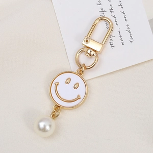 Detailed close-up of a gold alloy flower keychain with smile face and large pearl bead