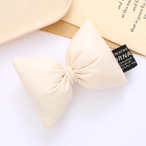 Minimalist cream leather bow accessory with black woven label for bags and shoes