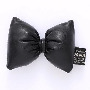 Macro detail of black faux leather bow accessory with textured finish and side woven label
