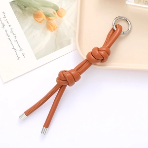 Close-up of brown leather knotted keychain with silver ring on a minimalist tray