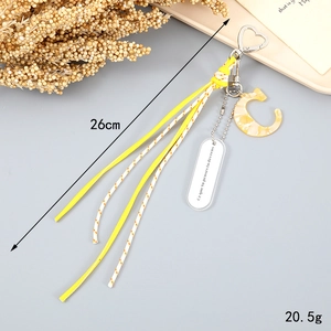 Detail of yellow tassel keychain with letter C pendant and engraved charm for handbags