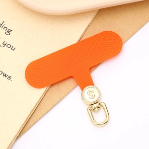 Macro detail of orange fabric phone tether tab with rotatable gold dollar sign metal hook