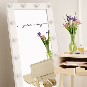 Black 'you look amazing' mirror sticker on a vanity mirror with warm lighting and cosmetics