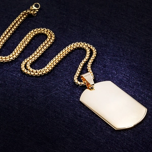Detail of gold military dog tag pendant with thick venetian box chain on blue fabric