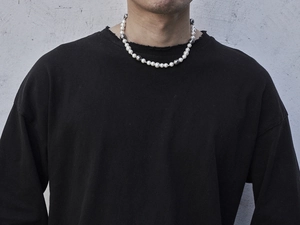 Detail of a unisex pearl necklace with grey beads on a male model in streetwear style