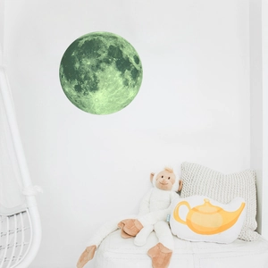 Luminous moon wall sticker glowing green on white wall in a cozy nursery room setting