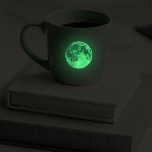 Luminous glow-in-the-dark moon design on dark ceramic mug in a low light environment