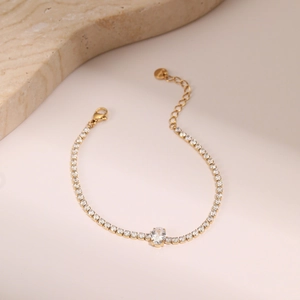 Detalle de una pulsera tennis dorada con piedra central ovalada y cierre de mosquetón