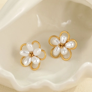 Détail de boucles d'oreilles fleur avec pétales dorés et cœurs de perles sur plateau blanc