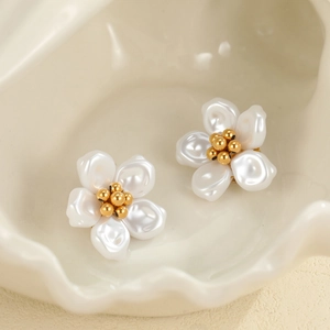 Détail de boucles d'oreilles fleurs nacrées blanches avec centre doré sur un plateau