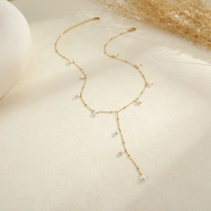Detalle de un elegante collar de lazo dorado en Y con pequeñas perlas blancas
