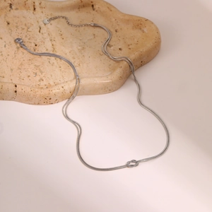 Zilveren dubbele slangenketting met knoop hanger op een beige dienblad met textuur