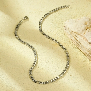 Detailed close-up of a silver Figaro chain necklace with a lobster clasp on a stone surface