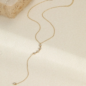 Detalle del collar lariat dorado con borlas de circón y cadena en O sobre fondo con textura