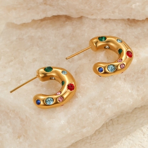 Detalle de pendientes en forma de C dorados con circonitas de colores sobre piedra