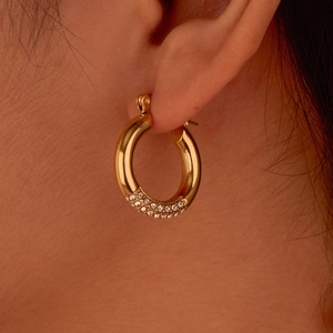 Detalle macro de pendientes de aro dorados en forma de C con circonitas en la modelo