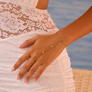 Elegante bracciale anello dorato con tre zirconi sulla mano di una donna in pizzo bianco