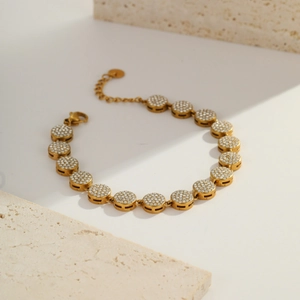 Detailed close-up of a gold-plated bracelet with zircon-encrusted circular links on stone