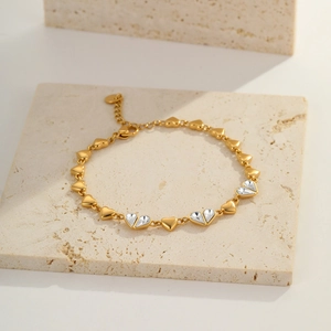 Detail of gold heart-link bracelet with zircon inlay on a beige travertine surface