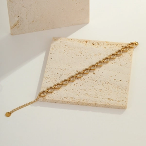 Close-up of golden heart-shaped linked bracelet with pavé zircon details on beige stone