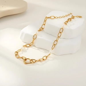 Macro detail of golden chain necklace with white pearls and heart toggle clasp on stone