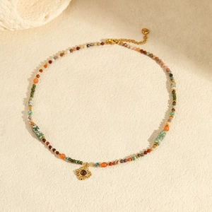 Detail of bohemian beaded necklace with golden sun pendant and gemstone on sand background