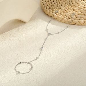 Detailed close-up of a silver heart zircon hand chain on a textured beige background