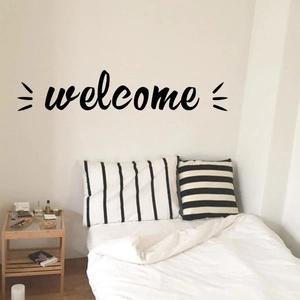 Detail view of a black Welcome wall sticker in script font on a bedroom wall decor