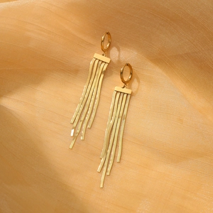Detailed macro of golden tassel earrings with snake chains on textured fabric