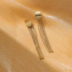 Close-up of golden geometric tassel earrings featuring sleek snake chains on silk fabric