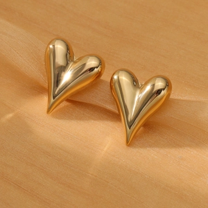 Detalle macro de pendientes de corazón 3D dorados sobre una elegante tela texturizada