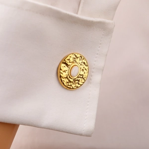 Macro detail of gold oval cufflink with white resin inlay and hammered texture on white cuff
